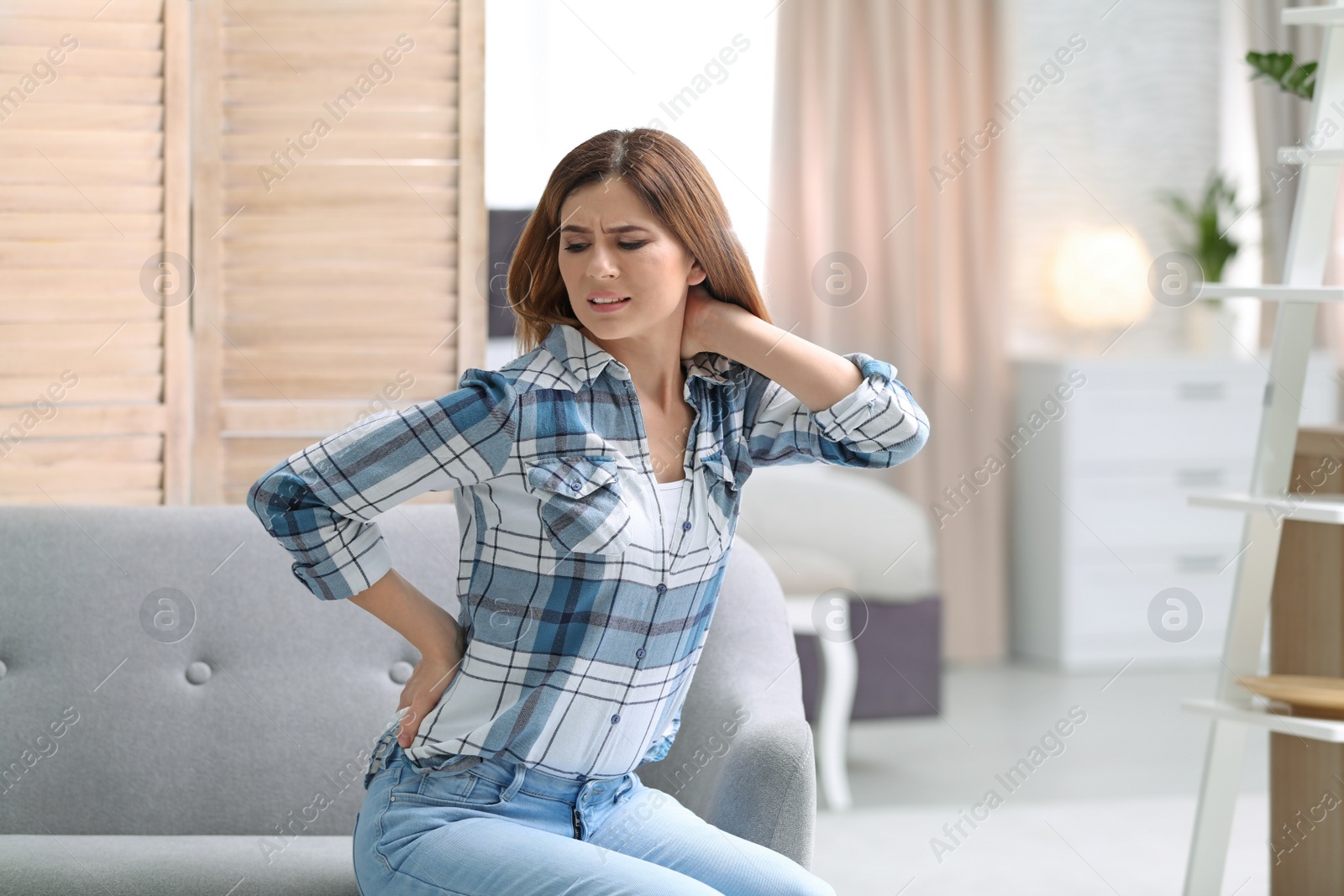 Photo of Young woman suffering from back pain at home