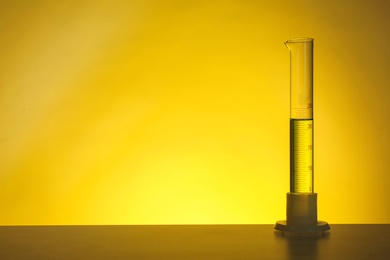 Graduated cylinder with liquid on table against color background. Chemistry laboratory glassware