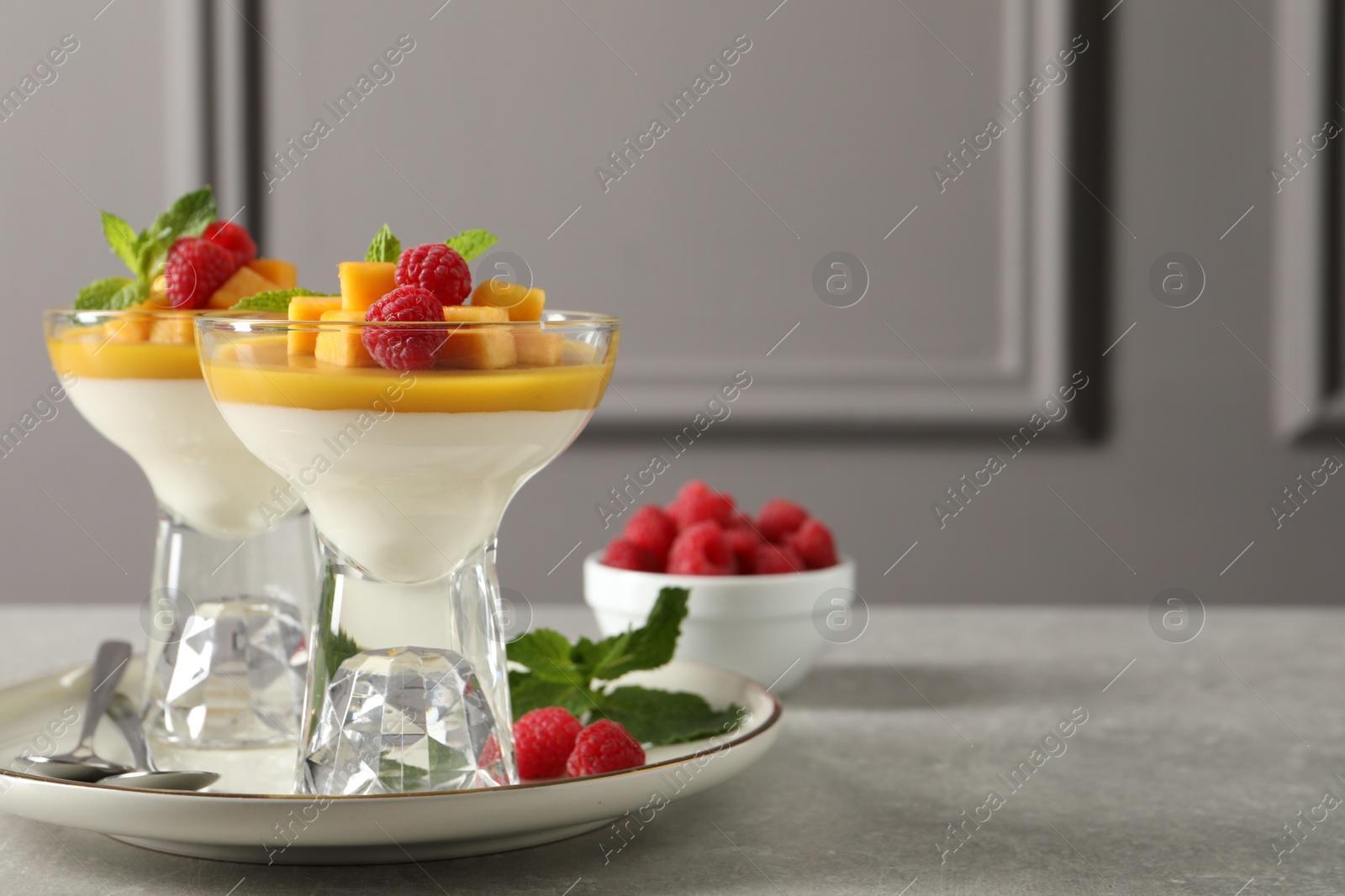 Photo of Delicious panna cotta with mango and raspberries on grey table. Space for text