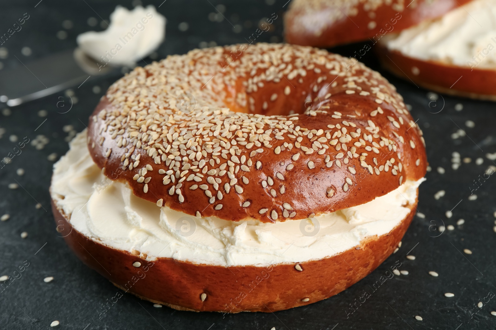 Photo of Delicious bagel with cream cheese on black table, closeup