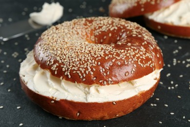 Delicious bagel with cream cheese on black table, closeup