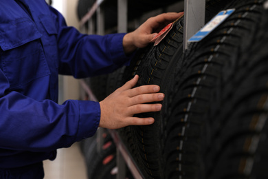 Photo of Male mechanic with car tire in auto store, closeup
