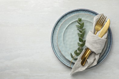 Photo of Stylish setting with cutlery, napkin, eucalyptus branch and plates on white table, top view. Space for text