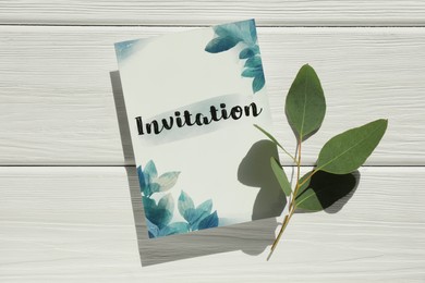 Photo of Beautiful card with word Invitation and green leaves on white wooden table, top view