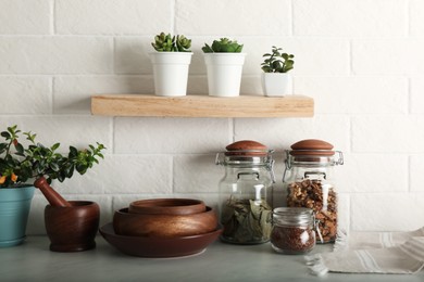 Wooden dishware and different products on grey table near white brick wall in kitchen