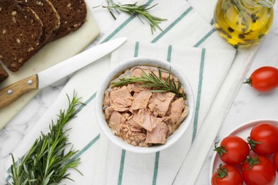 Bowl with canned tuna and products on white marble table, flat lay