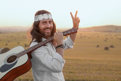 Photo of Happy hippie man with guitar showing peace sign in field, space for text