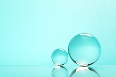 Transparent glass balls on mirror surface against turquoise background. Space for text