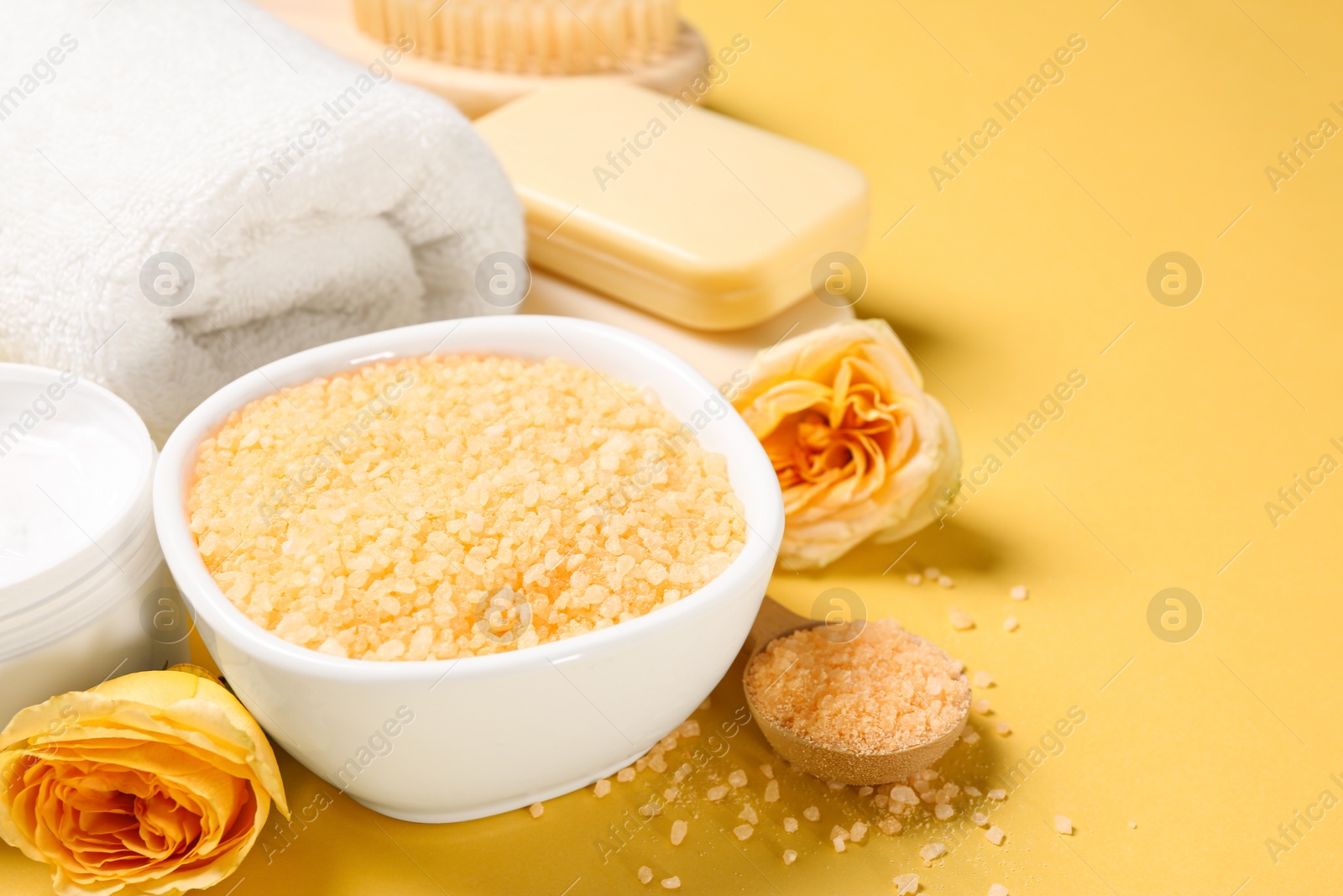 Photo of Bowl with sea salt, soap bars and beautiful roses on yellow background. Space for text