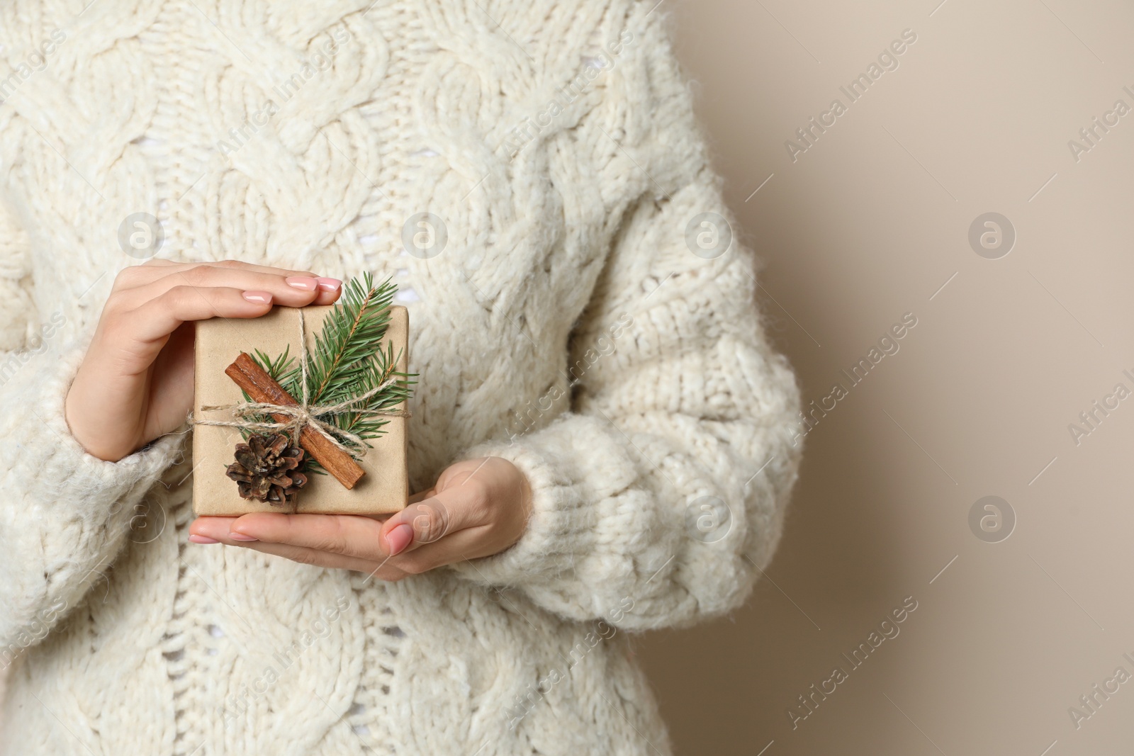 Photo of Woman holding beautifully wrapped Christmas gift box on beige background, closeup. Space for text