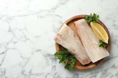 Photo of Fresh raw cod fillets with parsley and lemon on white marble table, top view. Space for text