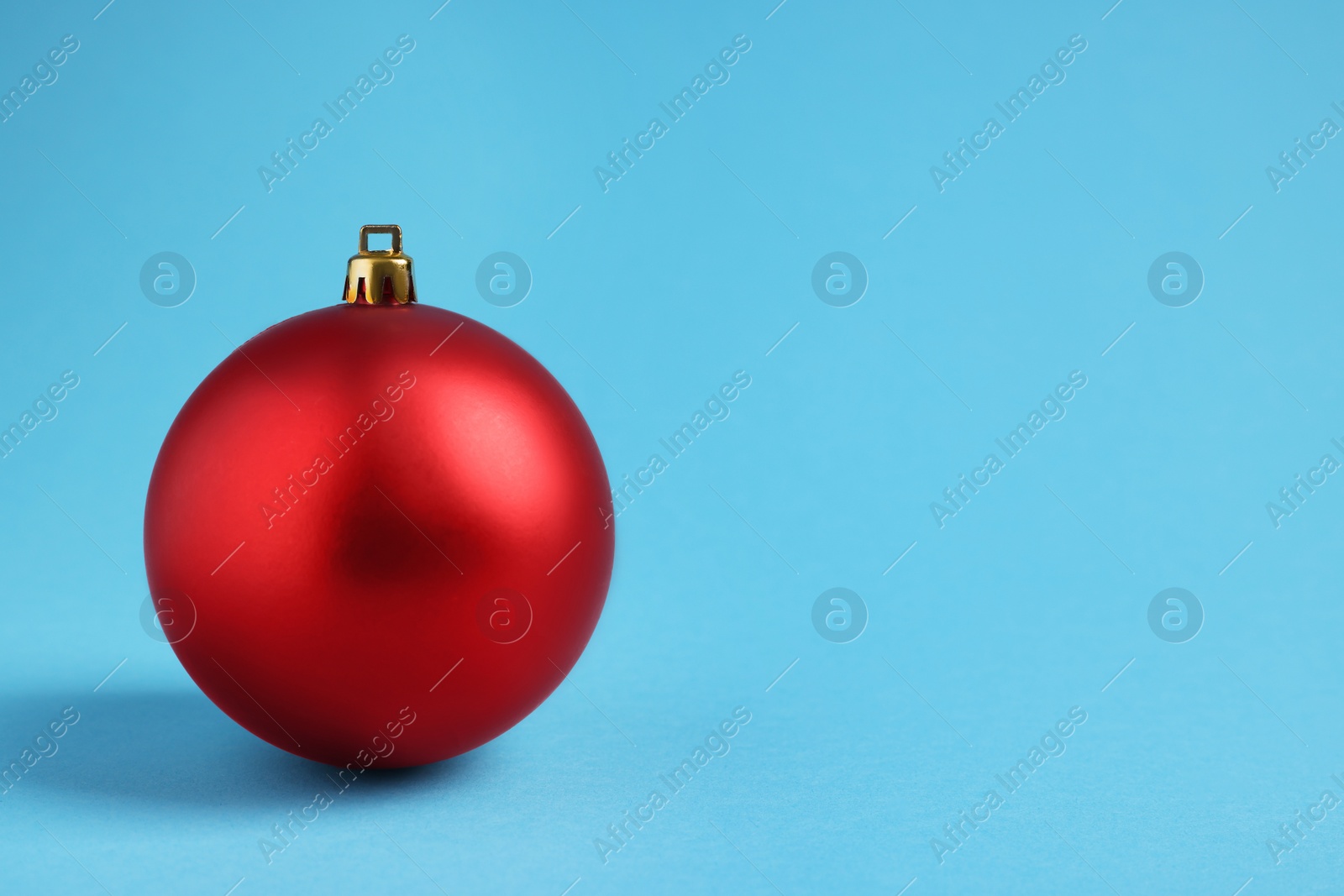 Photo of One red Christmas ball on light blue background. Space for text