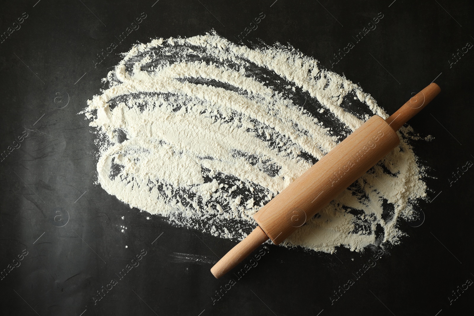 Photo of Scattered flour and rolling pin on black table, top view