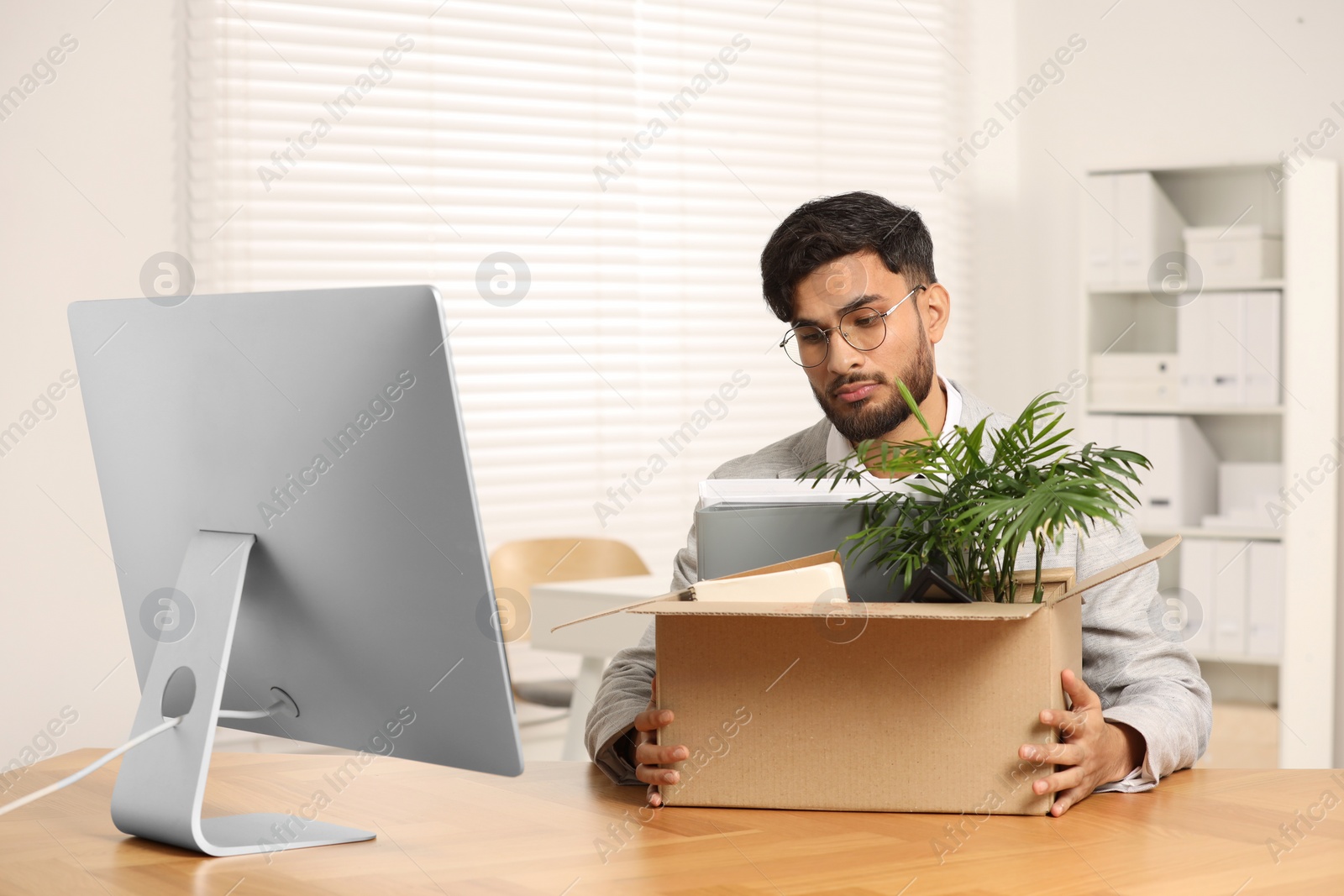 Photo of Unemployment problem. Frustrated man with box of personal belongings at desk in office