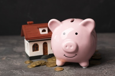 Photo of Piggy bank with pile of coins and house model on table