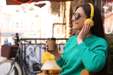 Photo of Happy young woman with coffee and headphones listening to music outdoors