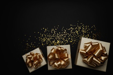 Golden gift boxes and confetti on black background, flat lay. Space for text