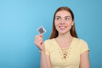 Photo of Woman holding condom on turquoise background, space for text. Safe sex