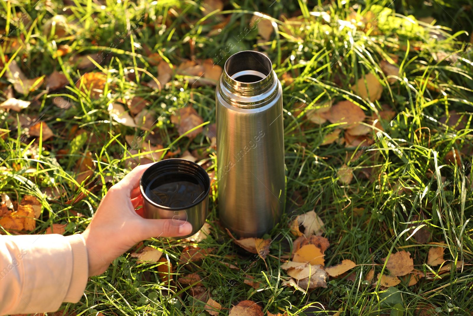 Photo of Woman with thermos and cup lid on green grass in autumn, closeup