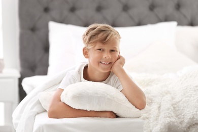 Cute little boy with pillow lying in bed at home