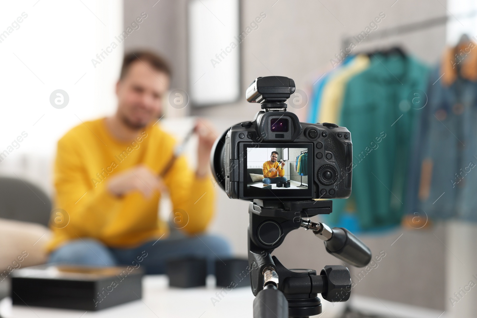 Photo of Fashion blogger showing wristwatch while recording video at home, focus on camera