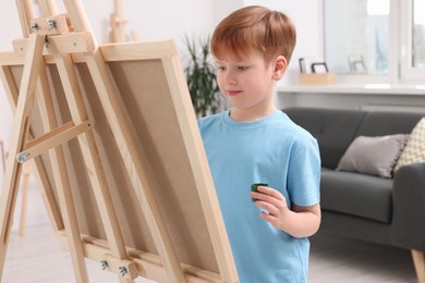 Little boy painting in studio. Using easel to hold canvas