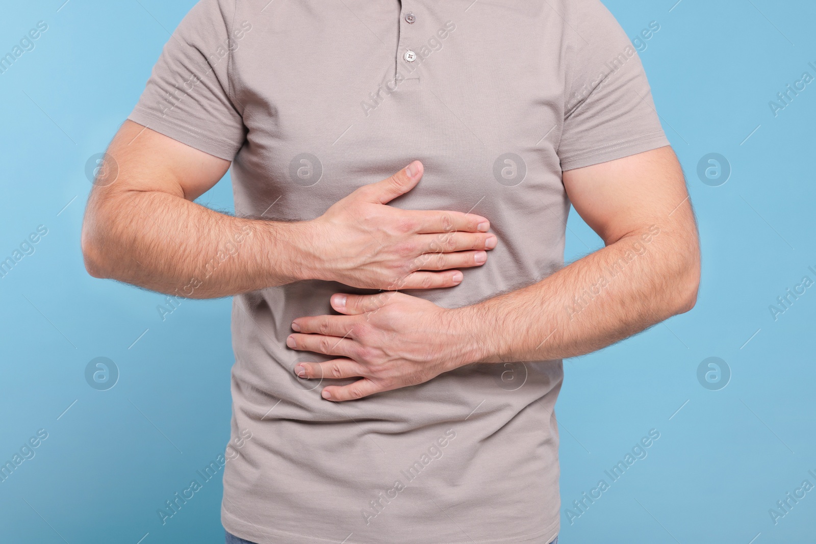 Photo of Man suffering from stomach pain on light blue background, closeup