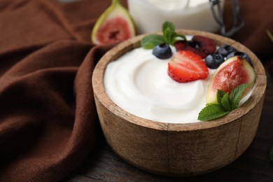 Bowl with yogurt, berries, fruits and mint on wooden table, closeup