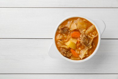 Photo of Tasty cabbage soup with meat and carrot on white wooden table, top view. Space for text