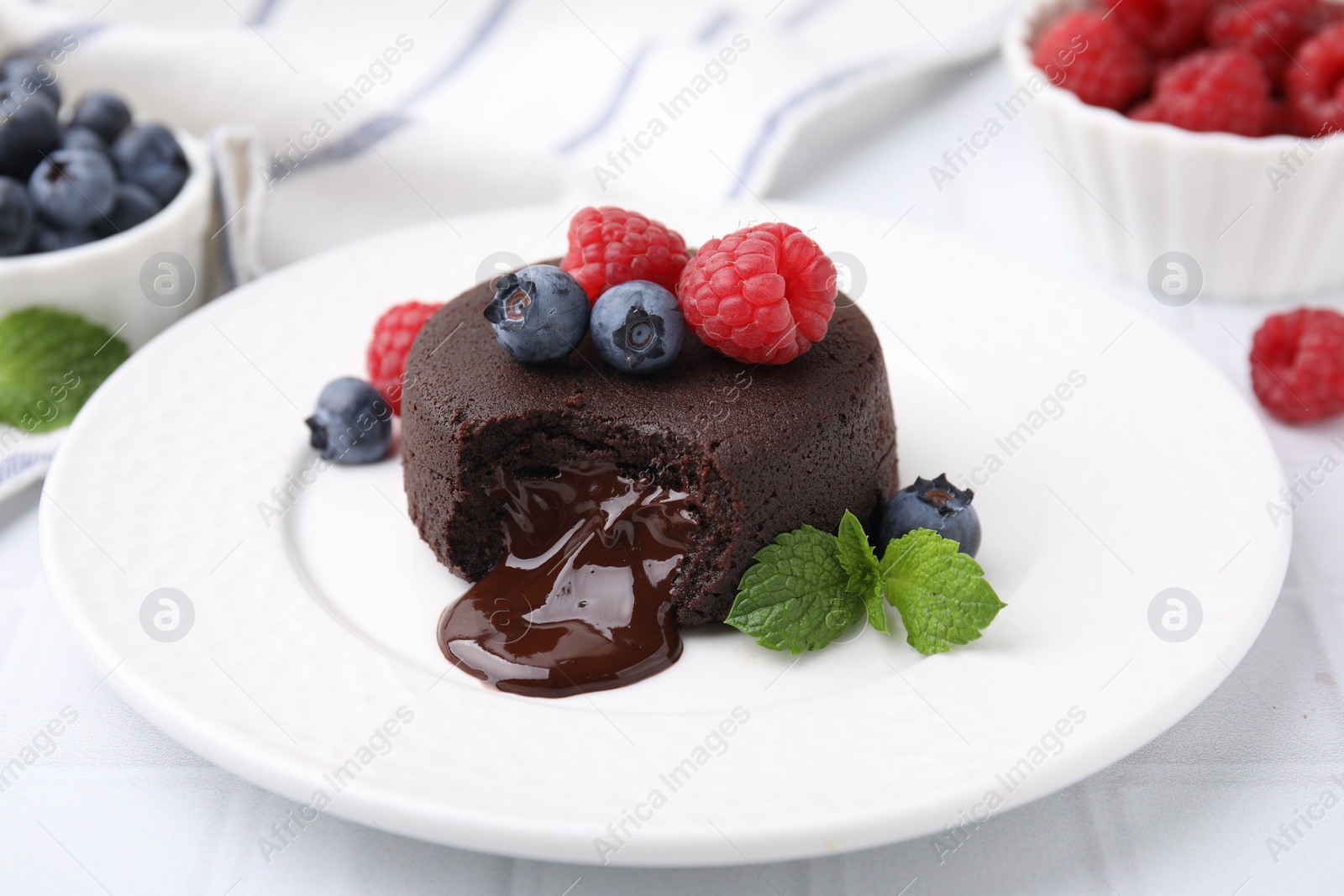 Photo of Plate with delicious chocolate fondant, berries and mint on white tiled table, closeup