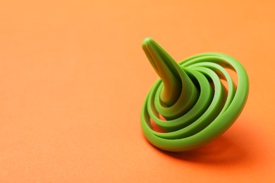 One green spinning top on orange background, closeup. Space for text
