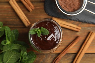 Photo of Glass of delicious hot chocolate with fresh mint and cinnamon sticks on wooden table, flat lay