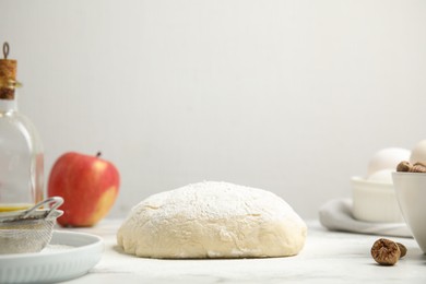 Photo of Raw dough, nutmeg seeds and other ingredients for pastry on marble table against white background