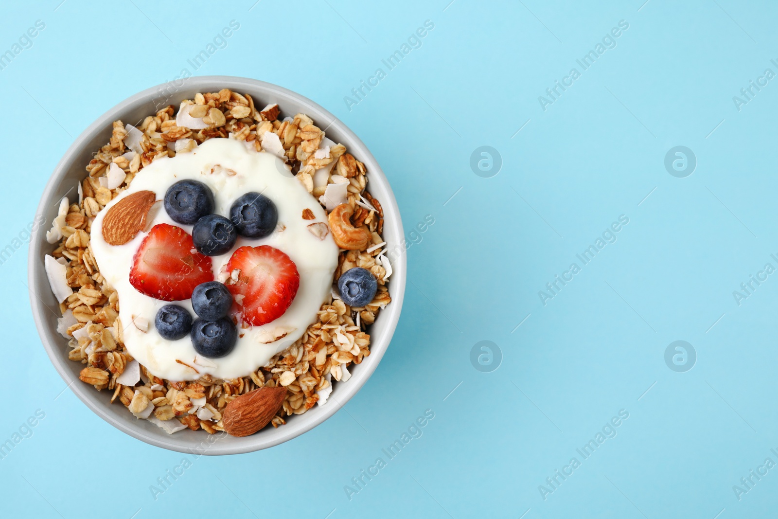 Photo of Tasty granola, yogurt and fresh berries in bowl on light blue background, top view with space for text. Healthy breakfast