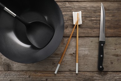 Photo of Black metal wok, chopsticks, knife and spatula on wooden table, flat lay