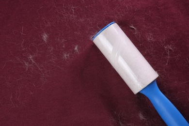 Lint roller on red fabric covered with hair, top view. Space for text