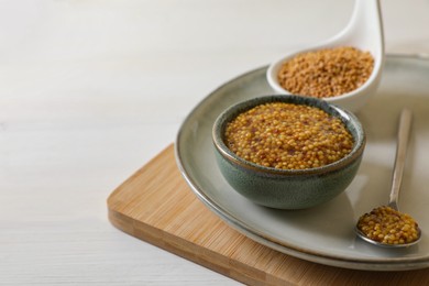 Photo of Bowl and spoon of whole grain mustard on white wooden table. Space for text