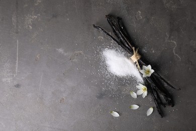 Photo of Vanilla pods, sugar, flowers and petals on gray textured table, flat lay. Space for text