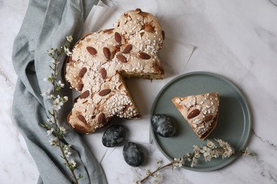 Delicious Italian Easter dove cake (traditional Colomba di Pasqua), painted eggs and branches with beautiful flowers on white marble table, flat lay