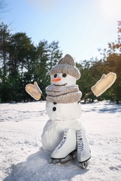 Photo of Funny snowman with hat, mittens and scarf in winter forest on sunny day