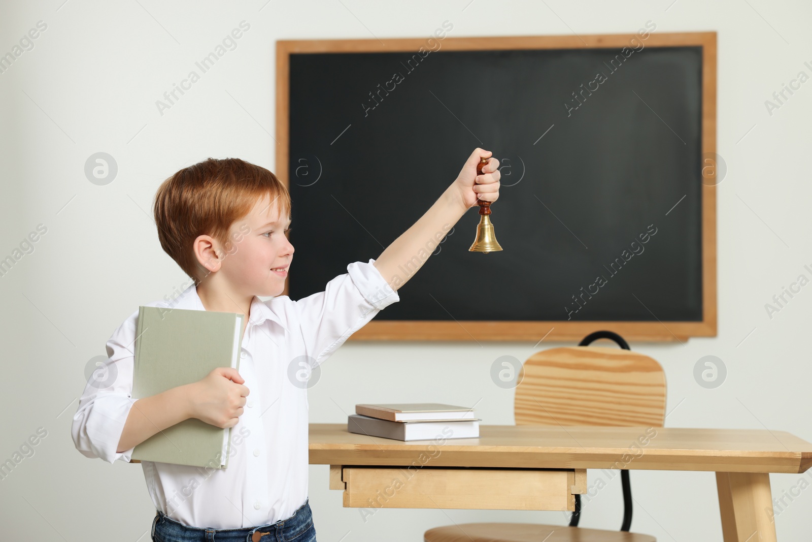 Photo of Cute little boy ringing school bell in classroom