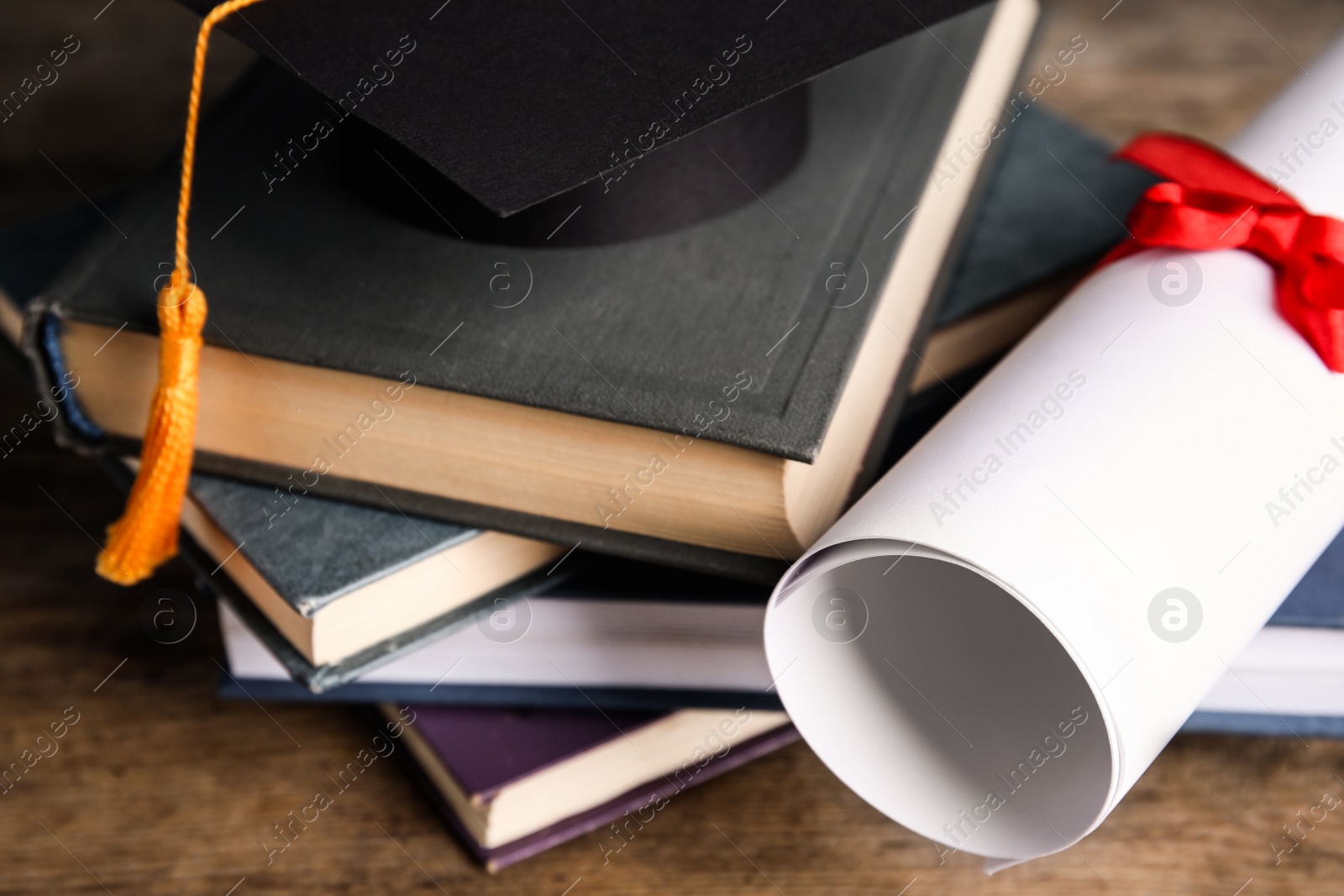 Photo of Graduation hat, books and student's diploma on wooden table, closeup