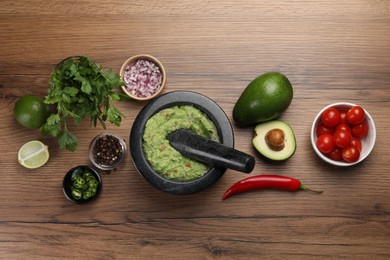 Delicious guacamole in mortar and ingredients on wooden table, flat lay