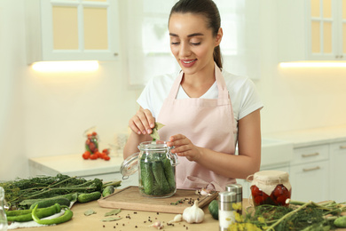 Woman putting bay leaves into pickling jar at table in kitchen