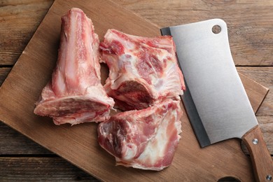 Photo of Cutting board with raw chopped meaty bones and butcher knife on wooden table, top view