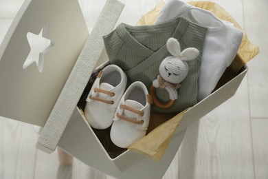 Photo of Box with baby clothes, shoes and toy on chair indoors, above view