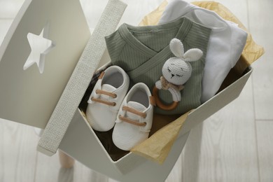 Box with baby clothes, shoes and toy on chair indoors, above view