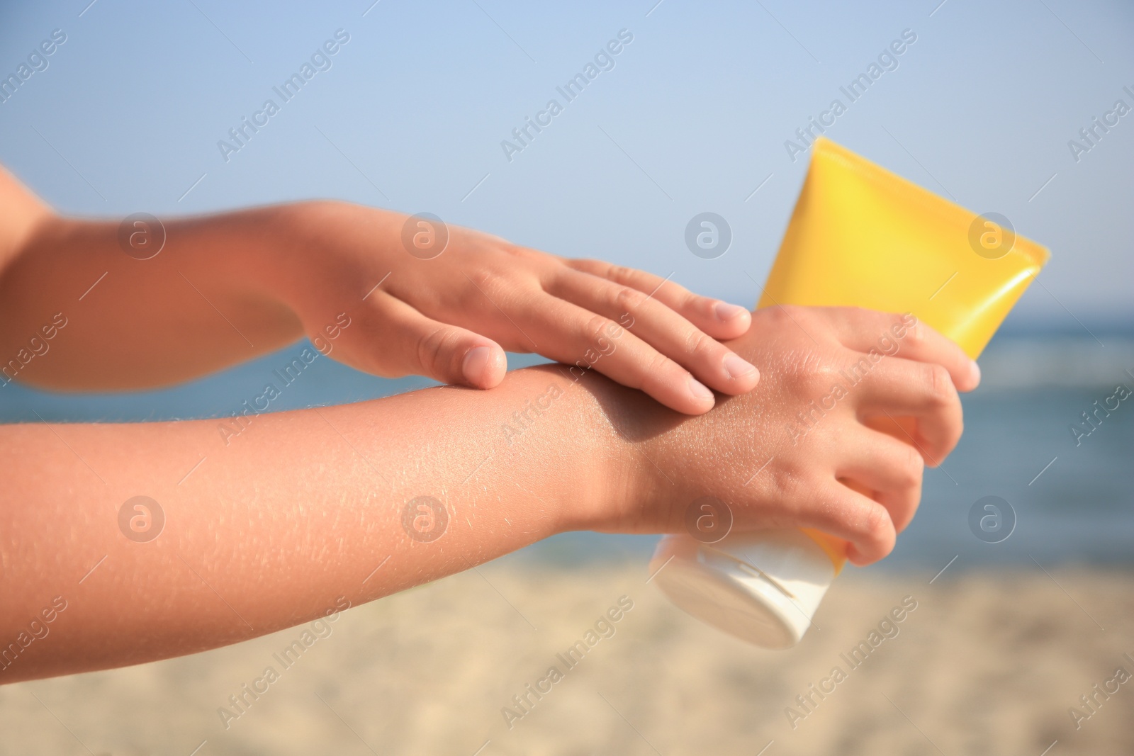 Photo of Child applying sunscreen near sea, closeup. Sun protection care