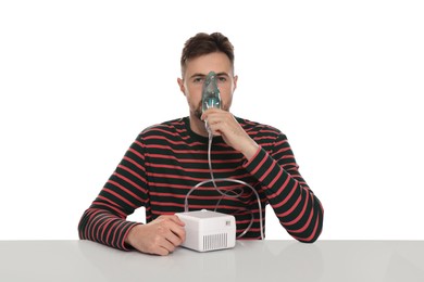 Photo of Sick man using nebulizer for inhalation at table on white background