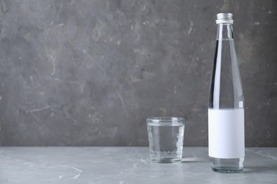 Photo of Bottle and glass with water on grey marble table, space for text